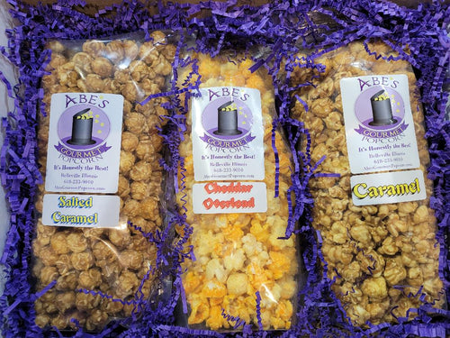 Contents of Cheddar Between the Sweets popcorn gift box.  1 bag of Salted Caramel popcorn, 1 bag of Cheddar Overload popcorn and 1 bag of Caramel popcorn.  All surrounded by paper crinkles and wrapped in tissue paper to make opening an experience. 